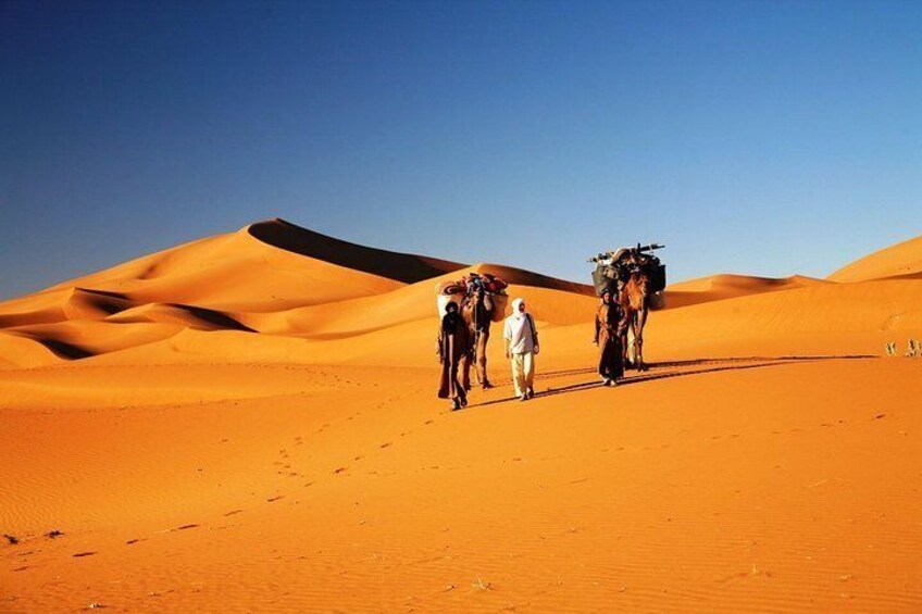 A group of people walking in a desert with sand dunes. 5