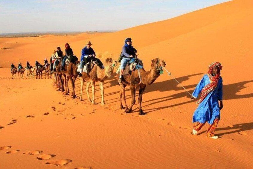 A group of people riding camels across a desert landscape. 1