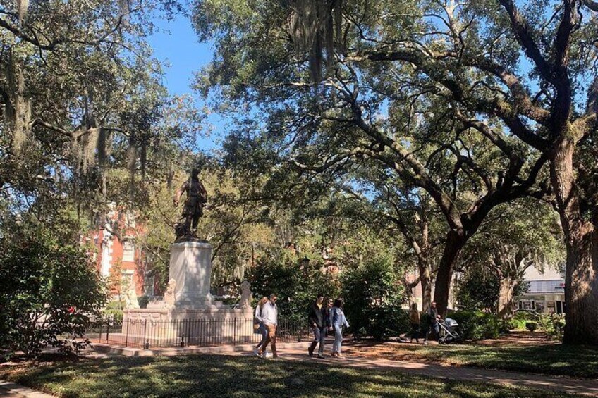 A park with a statue, large trees, and a building in the background. 2