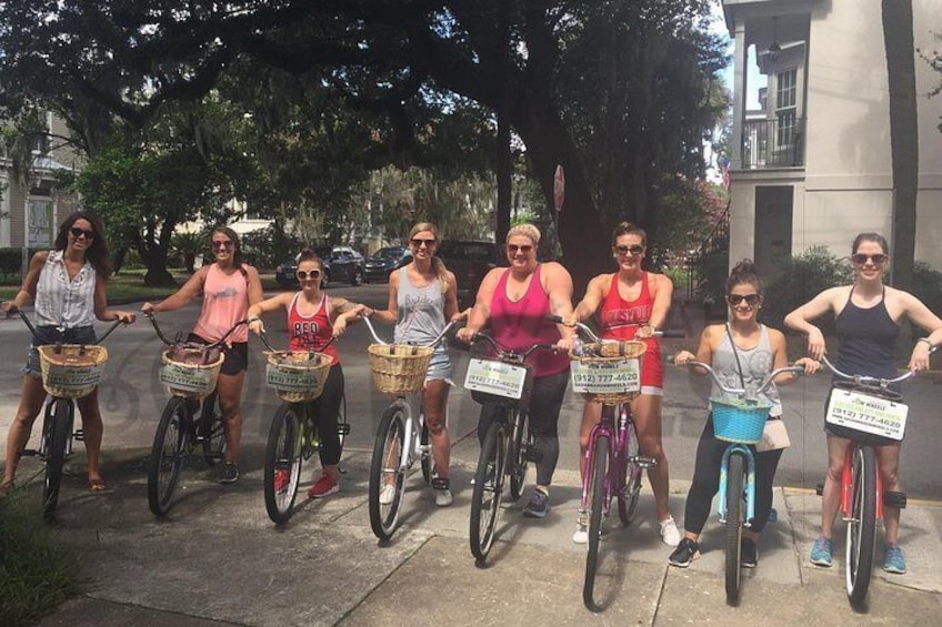 A group of people on bicycles with baskets, standing on a sidewalk. 3