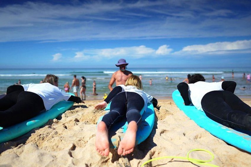 People lying on surfboards on a sandy beach with the ocean in the background. 2