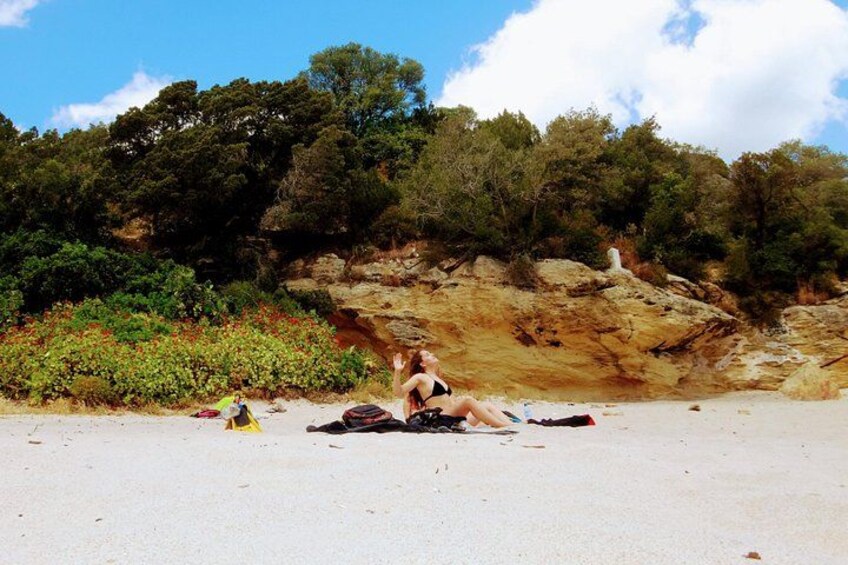 Una persona seduta sulla spiaggia, con una scogliera rocciosa e una vegetazione rigogliosa sullo sfondo. 4