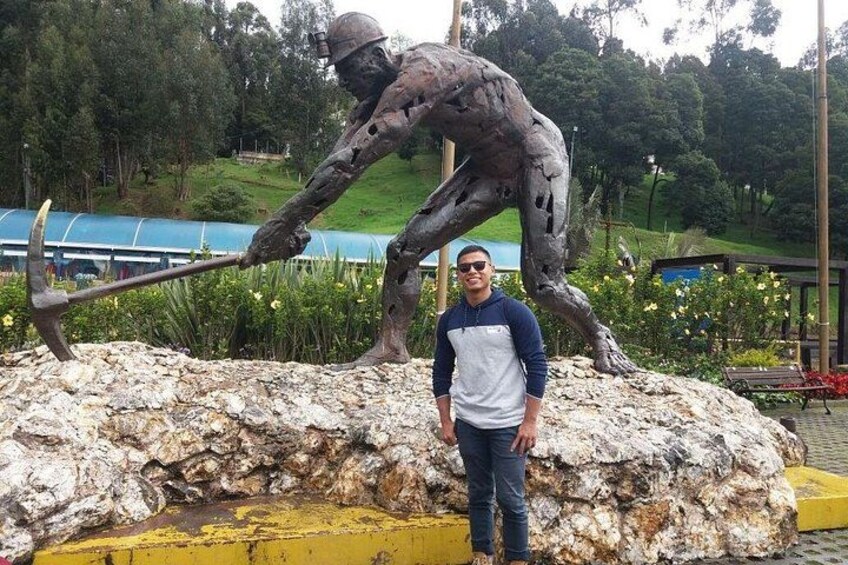 A man standing next to a large bronze statue of a miner with a pickaxe. 3