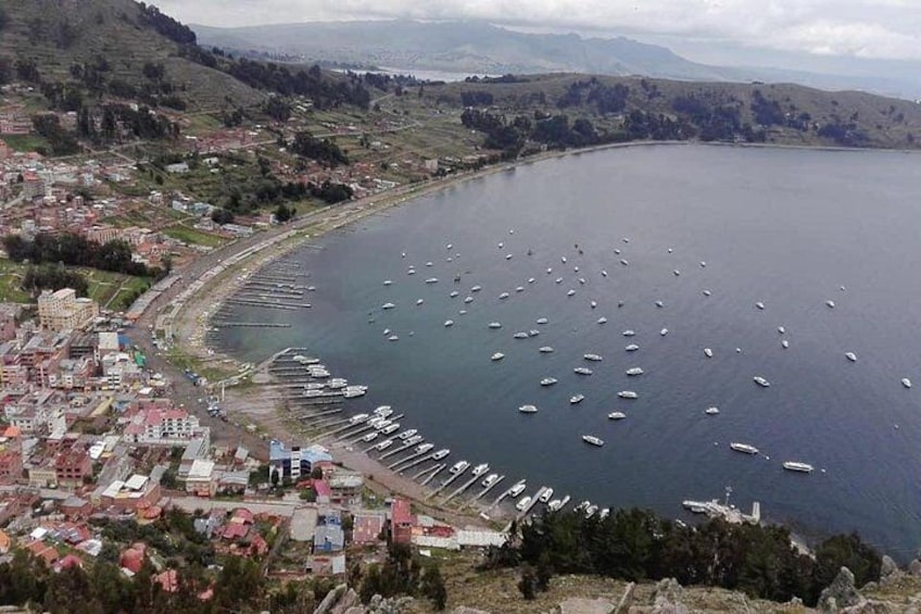 A coastal town with a marina filled with boats, surrounded by hills and a clear sky. 1