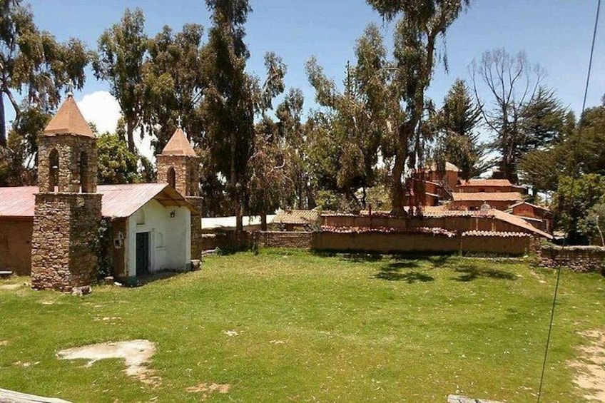 A grassy area with stone buildings, including a small chapel with a bell tower. 4