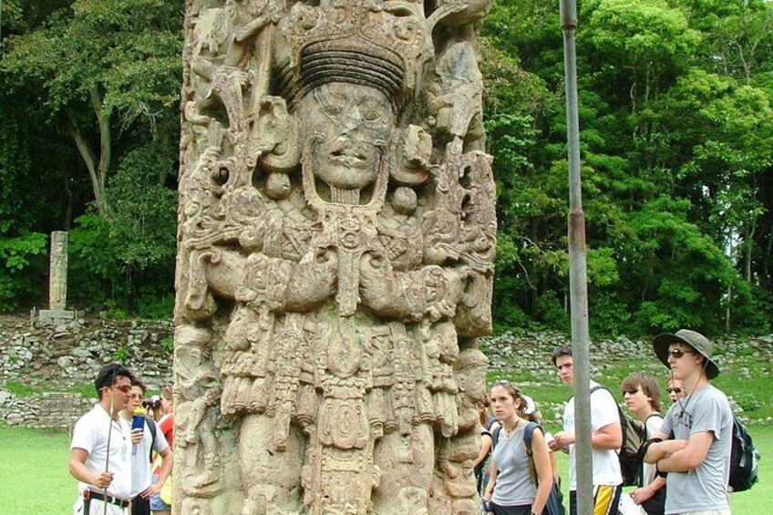 A stone carving with intricate details, surrounded by lush greenery and a few visitors. 2