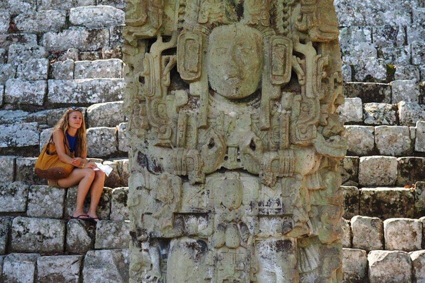 A person sitting on stone steps next to a detailed stone carving. 1
