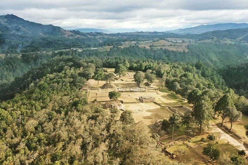 A rural landscape with a clearing surrounded by dense forest, a hill in the background, and a distant mountain range. 4