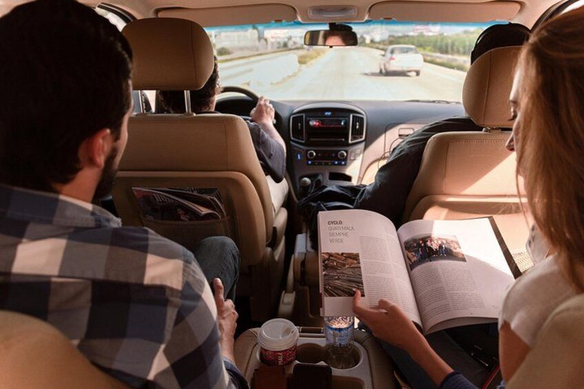 Two people reading books in a car with a road visible outside. 3