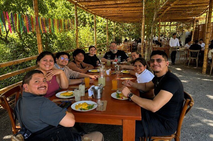 Un grupo de personas cenando al aire libre en una mesa de madera con comida y bebidas. 2