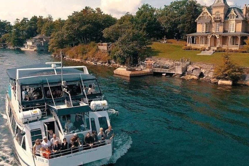 A boat with passengers on a river, surrounded by trees and a large house. 4