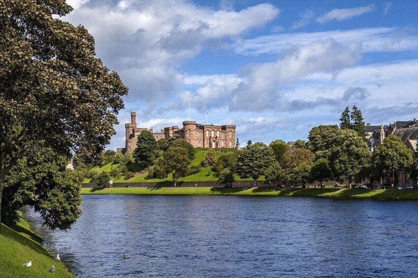 Un château perché sur une colline, un plan d’eau et un sentier bordé d’arbres. 1