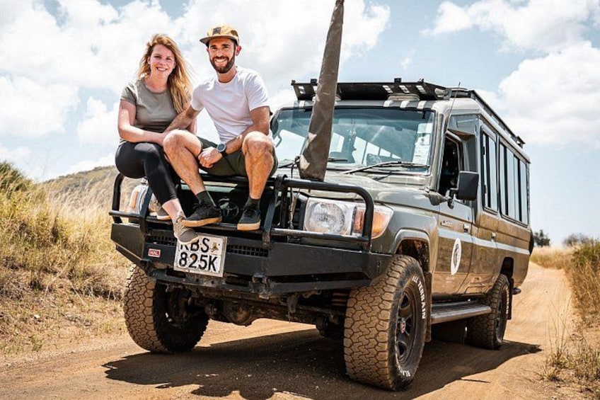 A couple sitting on a vehicle with a license plate '825K' on a dirt road. 2