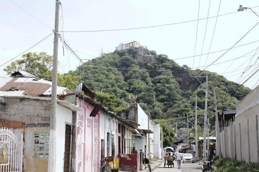 A street with buildings, a person walking, and a hill with a structure on top. 5