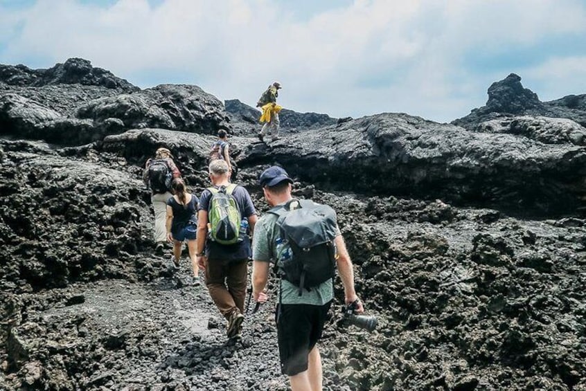 People hiking on a volcanic terrain with rugged rocks and a clear sky. 1