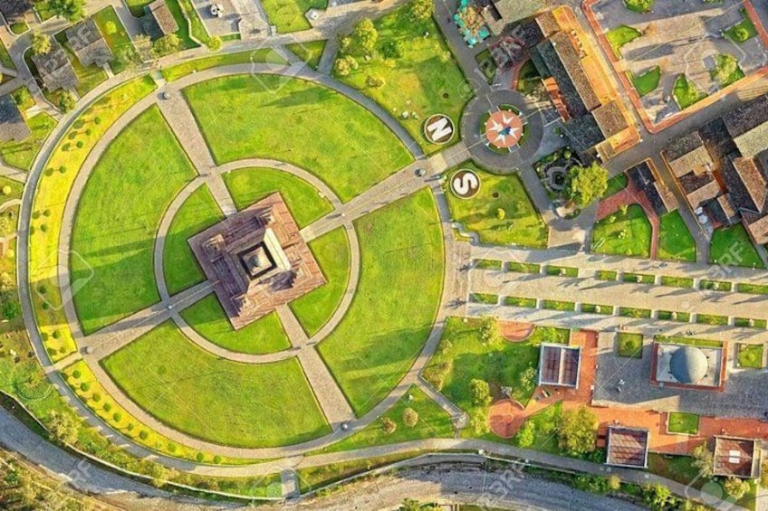 An aerial view of a circular park with a central monument, surrounding pathways, and adjacent buildings. 1