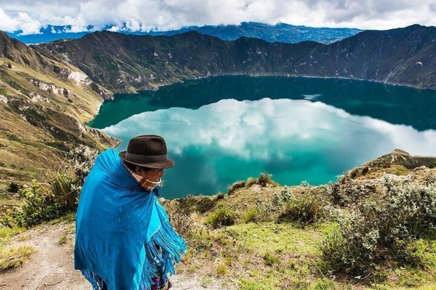 Una persona con un chal y un sombrero azules observa un lago turquesa rodeado de montañas. 1