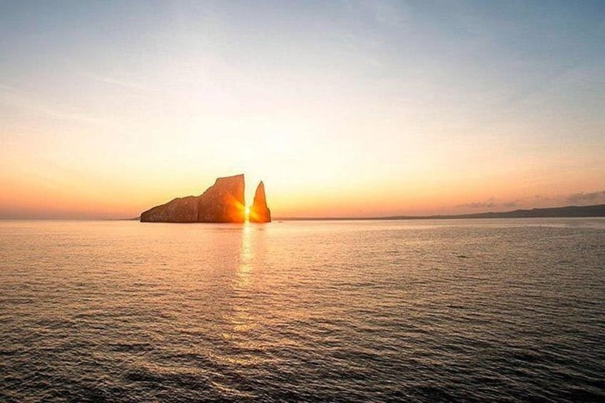 A calm sea at sunset with a large rock formation in the distance. 2