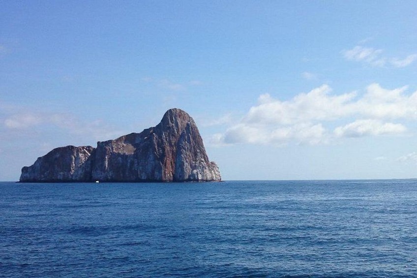A large rock formation in the ocean with clear blue water and a partly cloudy sky. 4