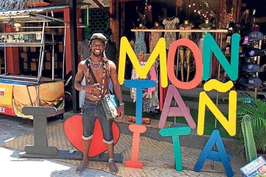 A person standing in front of a colorful sign with letters spelling 'MONTA'. 2