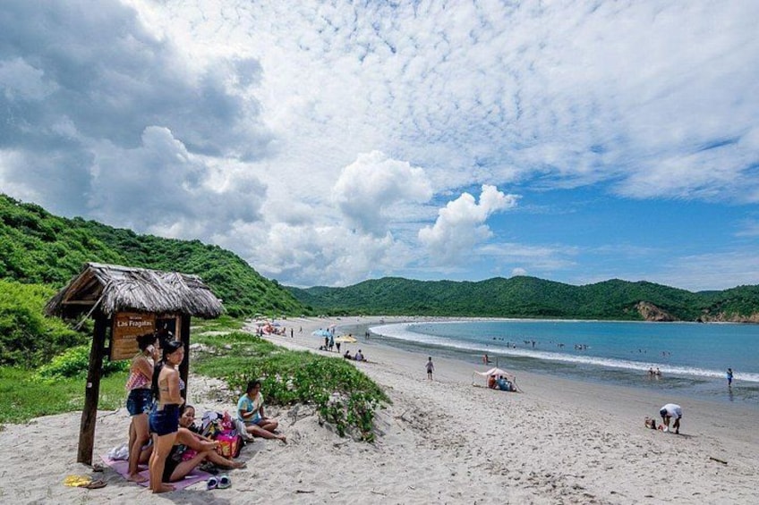 A beach with people sunbathing, a hut, and a clear sky. 3