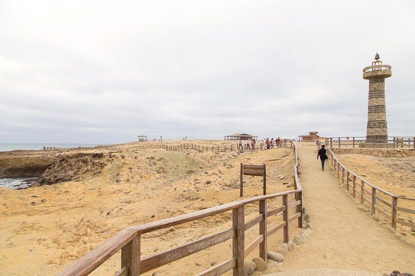 A sandy beach with a wooden walkway leading to a lighthouse. 4
