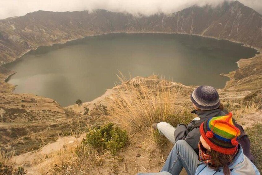 A person sitting on a hill overlooking a lake surrounded by mountains. 4