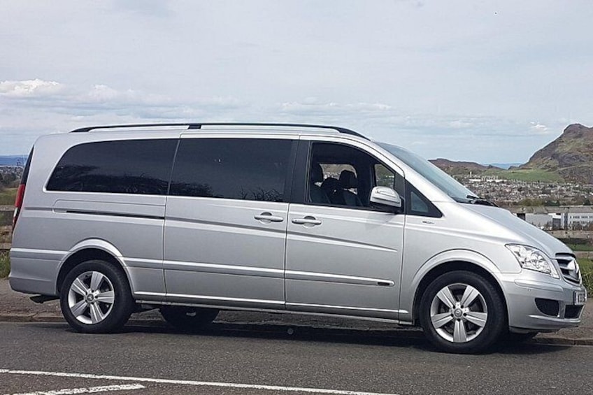 En sølvgrå minivan parkeret på en vej med et bjergrigt landskab i baggrunden. 3
