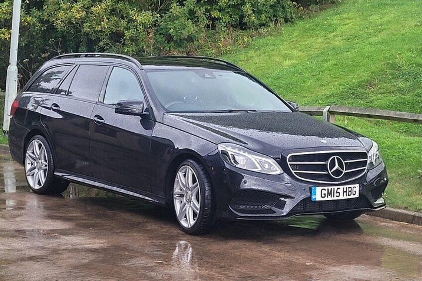 En sort Mercedes-Benz stationcar parkeret på en våd vej med en græsplæne og et træhegn i baggrunden. 4
