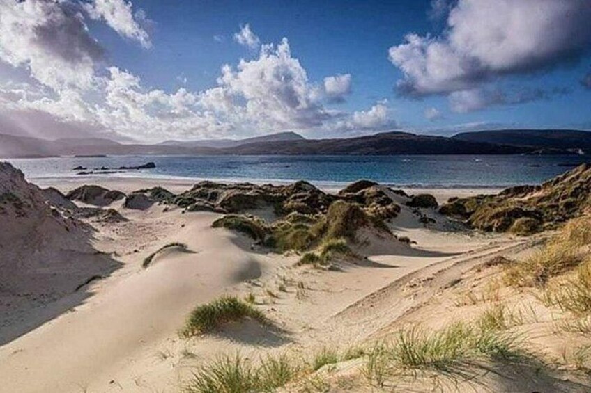 Un paysage côtier avec des dunes de sable, une plage et une mer calme sous un ciel partiellement nuageux. 5