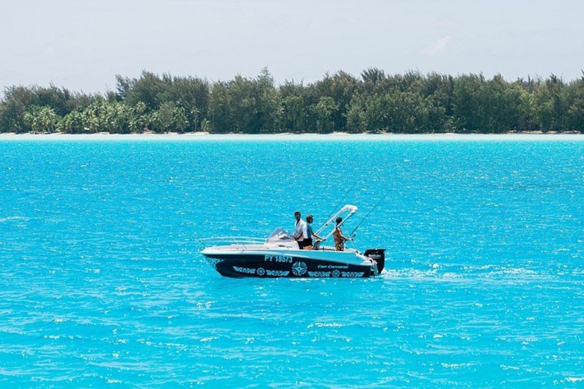 Een snelboot op turquoise water, met een bebost eiland op de achtergrond. 2