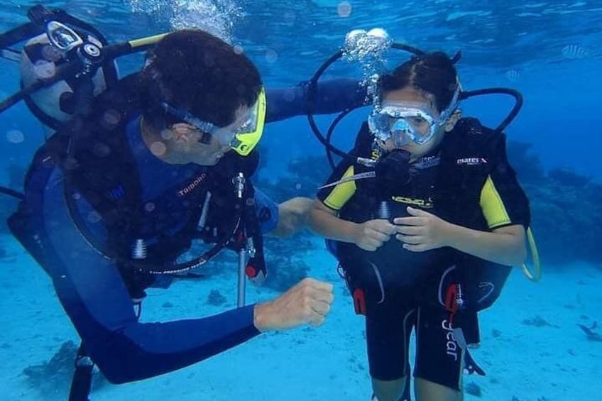 Two scuba divers underwater, one assisting the other with their equipment. 1