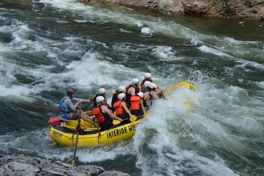 A group of people in a yellow inflatable raft navigating through a river with rapids. 5