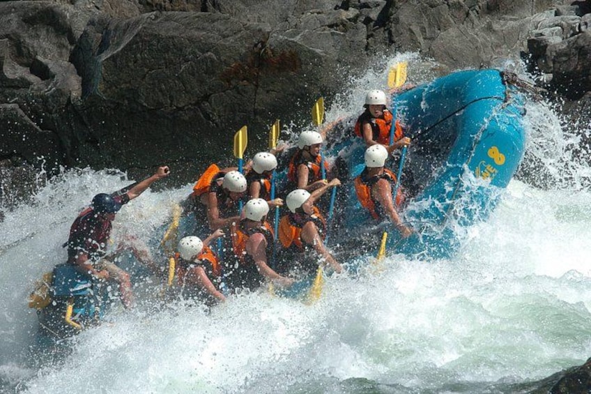 A group of people in a blue raft navigating through a turbulent river. 1