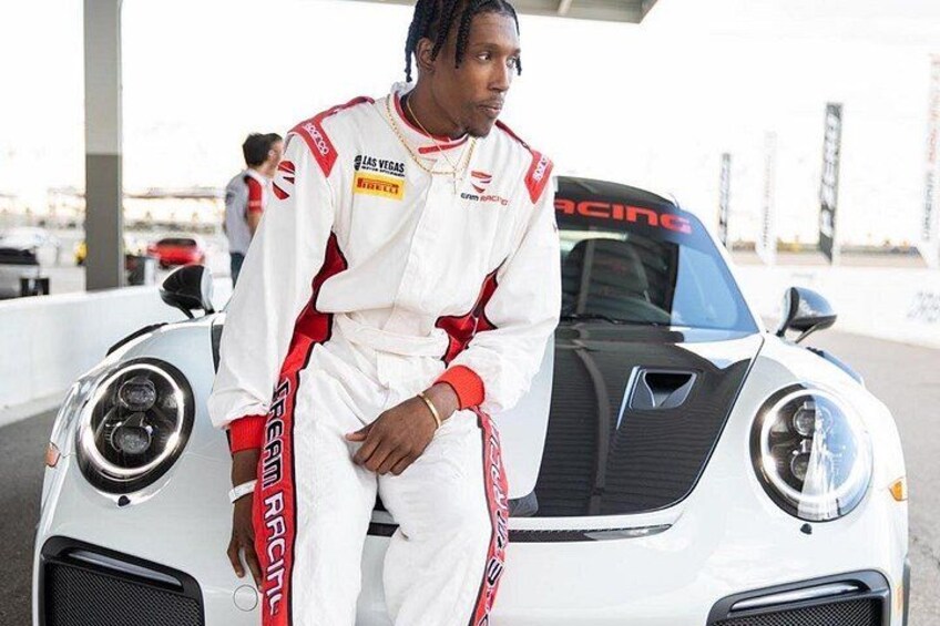 A person in a racing suit standing next to a white sports car with racing decals. 1