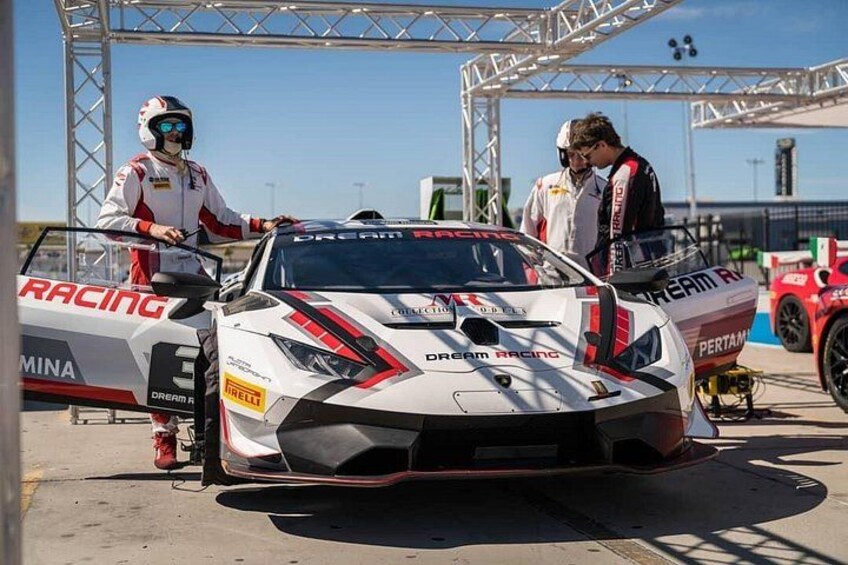 A racing car with 'Dream Racing' and 'Pirelli' logos, a person in racing gear, and another person in a white suit. 2