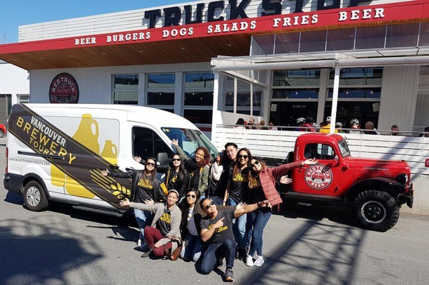 Un gruppo di persone che posa davanti a un food truck e a un edificio con un cartello che riporta la scritta 'TRUCKS FRIES BEER'. 2