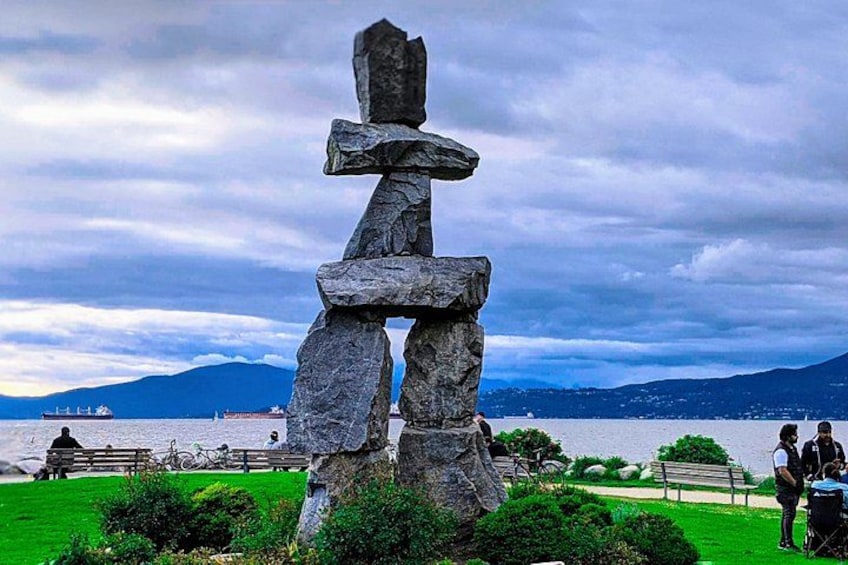 A totem pole in a park with a lake and mountains in the background. 5
