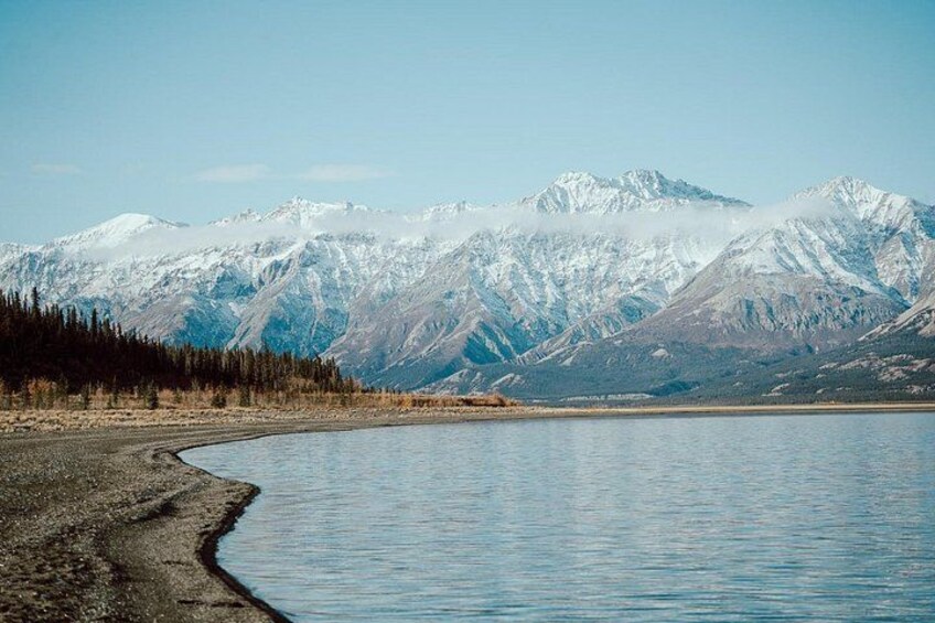 Un lago con una orilla sinuosa, rodeado de montañas nevadas y una zona boscosa. 1
