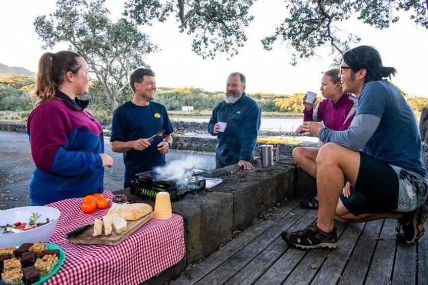 A group of people gathered around a barbecue grill outdoors, with food and drinks on a table. 4