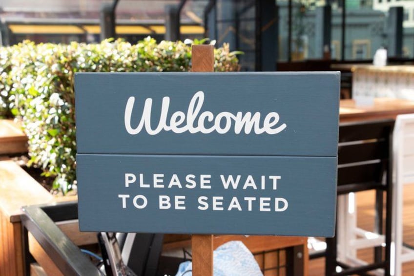 A wooden sign with 'Welcome' and 'Please wait to be seated' written on it. 3