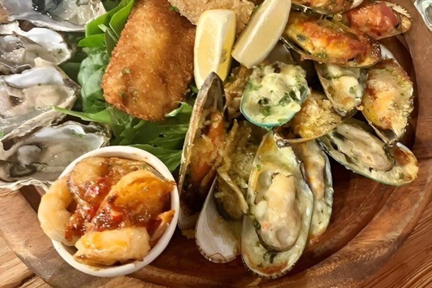 A seafood platter with oysters, clams, and a breaded item, possibly a fish, on a wooden board. 2
