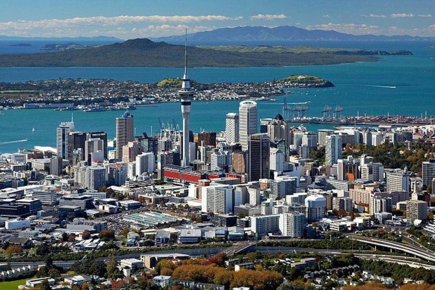 A cityscape with a prominent tower, dense urban buildings, and a body of water in the background. 4