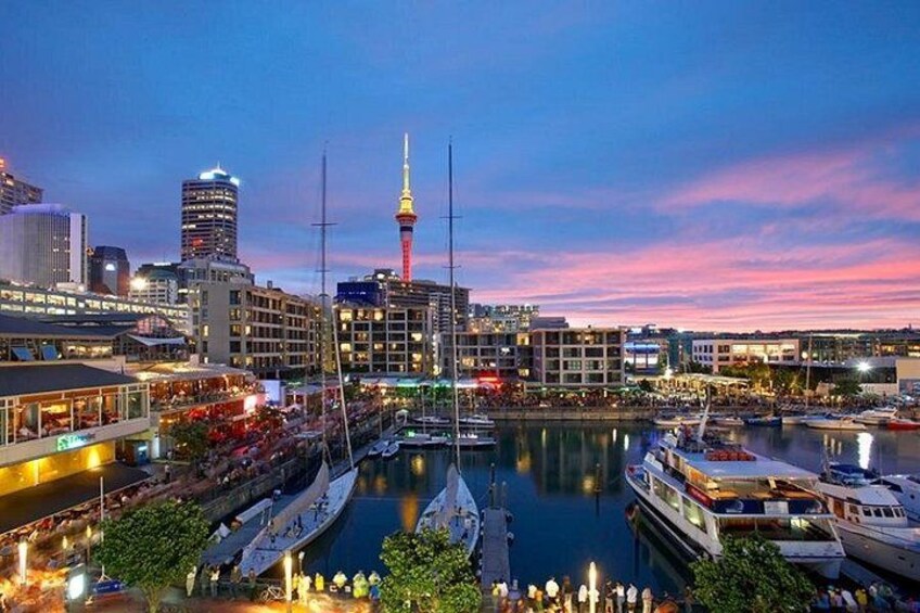 A cityscape at dusk with a prominent tower, waterfront, and marina. 1