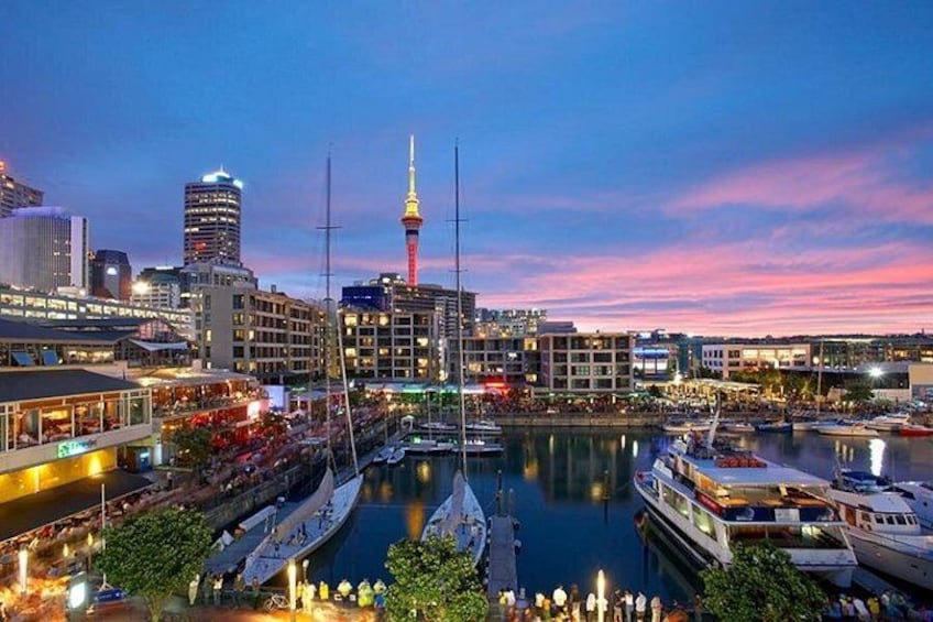A cityscape at dusk with a prominent tower, waterfront, and marina. 5