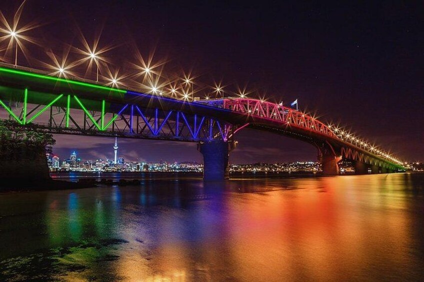 A brightly lit bridge at night with colorful lights reflecting on the water. 2