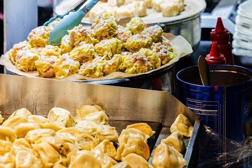 A variety of dumplings on a tray, a blue canister, and a red condiment bottle. 1