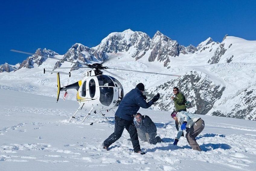 A helicopter on a snowy mountain with people around it. 1