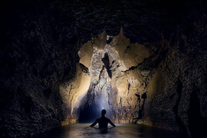 En grotta med stalaktiter och stalagmiter, en person som sitter i mitten och en ljuskälla som lyser upp grottan. 5