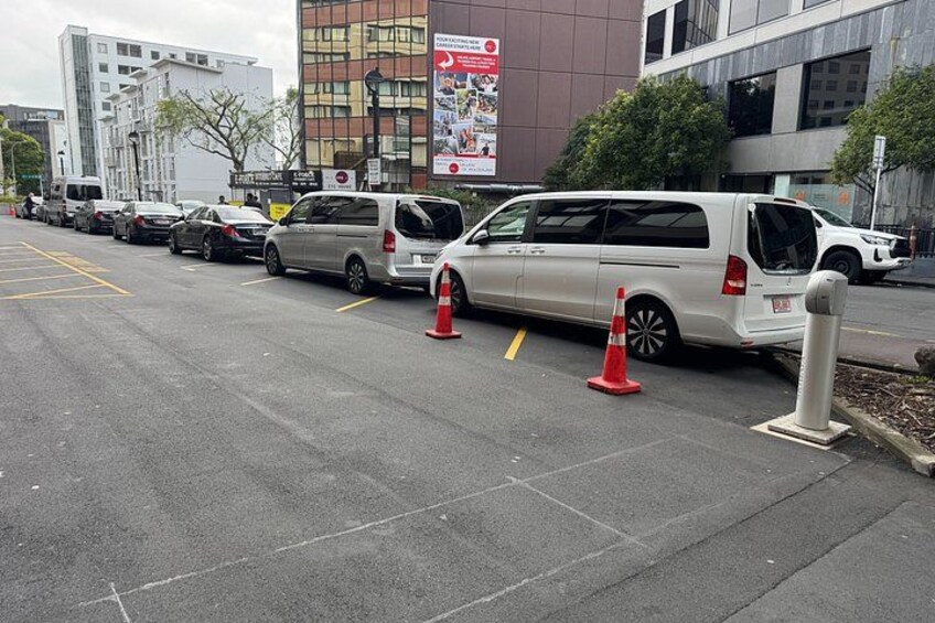 A parking lot with several cars and a white van, traffic cones, and a building with advertisements. 2